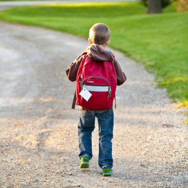 kid walking away with a backpack on walking on a dirt path.
