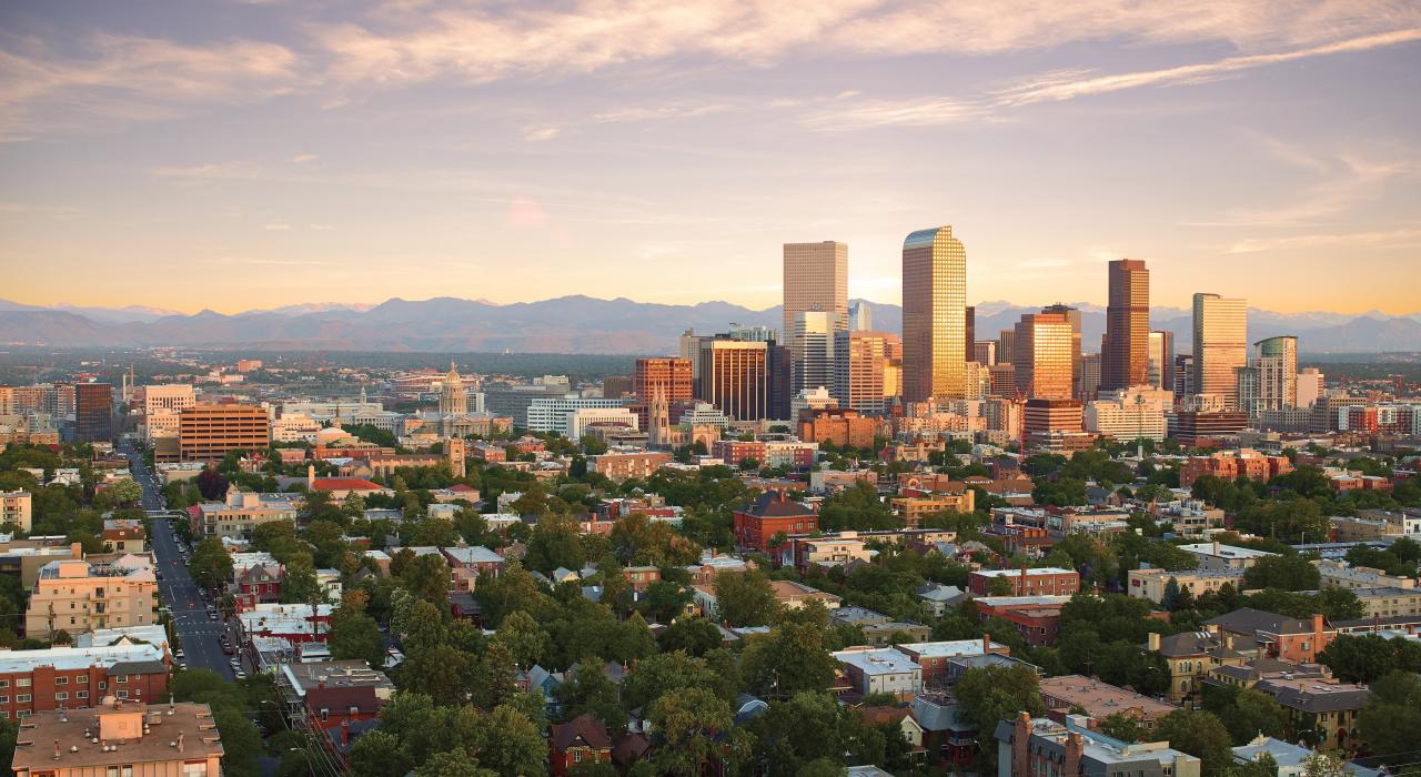 Skyline image of downtown denver with high rise buildings and the mountains in the background and neighborhood houses in the foreground